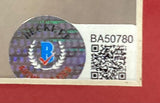 A close-up of the Sports Integrity security hologram sticker with a blue B and laurel leaves, plus code BA50780 and QR code, on the 50 Cent Signed Framed 8x10 Photo BAS. White background with red border.