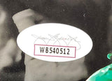 Close-up of a white oval JSA sticker, code WB540512, on a Jeremiah Trotter Jr signed 8x10 Philadelphia Eagles Spotlight Photo by Sports Integrity; sticker features bold black text in a red-bordered rectangle against a blurry monochrome background.