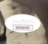 Close-up of an oval JSA sticker with the code WB540553, attached to a Jeremiah Trotter Jr Signed in Green 11x14 Philadelphia Eagles Spotlight Photo by Sports Integrity. A faint signature and part of a torso are visible in the blurry background.