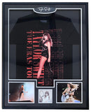 The Sports Integrity T Swift Framed Swift Eras Tour Shirt features a signed insert authenticated by PSA/DNA, a black T-shirt, a large concert photo of Taylor Swift performing, two smaller photos, and a signature plaque.
