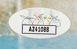 An oval sticker with a faded background features an illegible signature above bold code AZ41088 on white, authenticating the Adam Sandler Signed Framed 8x10 Billy Madison Singing Photo by Sports Integrity.