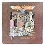 The Aerosmith Toys in the Attic 1975 Vinyl Record 4 by Sports Integrity features cover art with animated toys in an attic, the band’s logo at the top, and album title at the bottom on a brown background.
