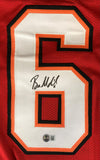 A large white and orange number 6 is printed on a red Baker Mayfield Tampa Bay football jersey. Signed in black marker with an authentication sticker, this jersey is offered by Sports Integrity and authenticated by BAS.