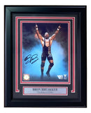 A signed and framed 8x10 WWE photo of wrestler Bron Breakker in a black checkered singlet, arms raised, from Sports Integrity. Features authentication logos and a plaque reading “Bron Breakker The Badass of WWE.”.