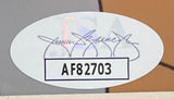 An oval Sports Integrity sticker with a decorative signature appears above a rectangular box displaying code AF82703 in bold black on a smooth, multicolored surface of the Cheech & Chong Signed Framed 8x10 The Simpsons Photo JSA.