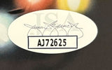 An oval sticker with a printed signature above bold black serial AJ72625 inside a rectangle, faint JSA letters in back, appears on the Sports Integrity Chevy Chase Signed Framed 11x17 Lampoon’s Christmas Vacation Photo.