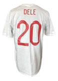 A white Sports Integrity Dele Alli Signed England Soccer T-Shirt Jersey ICONS, with “DELE” and red number “20” on the back and an autograph on the number.