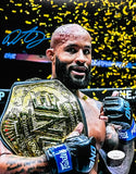 The Sports Integrity Demetrious "Mighty Mouse" Johnson Signed 8x10 UFC Photo (JSA) shows Johnson, bearded, with a gold belt over his shoulder and black-blue gloves, as gold confetti falls. His blue autograph appears at the top left.