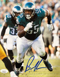 Brandon Graham runs on the field in a green Eagles jersey (#55) during a game, with teammates and an opponent in yellow visible behind him. This 8x10 Sports Integrity photo features his blue autograph at the bottom. JSA authenticated.