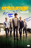 Five stylish men walk confidently by luxury cars under a dramatic sky. The image features the Entourage The Movie title and blue autographs. Product: Entourage Cast Signed 11x17 Movie Photo by Sports Integrity, includes Adrien Grenier & others, JSA certified.
