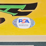 A close-up of a PSA AG85259 authentication sticker appears on the yellow and green background of the Giannis Antetokounmpo Signed Framed 8x10 Milwaukee Bucks Photo by Sports Integrity.