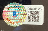 Close-up of a Sports Integrity holographic AUTHENTICATED sticker with blue and red logo, overlapping a white label with QR code and alphanumeric BD88125, on the Charlie Hunnam Labrava Signed Framed 11x14 Sons Of Anarchy Jax Happy Photo BAS.