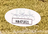 Close-up of an oval sticker on grass, showing barcode WA471821 with a faint blue signature above, from the Sports Integrity Jalen Hurts SB LIX MVP Signed Framed 16x20 Eagles Run Photo Fly Eagles Fly JSA.