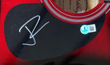 A close-up of the Sports Integrity Jelly Roll Signed 41" Red Acoustic Guitar shows its black pickguard with a white signature and a blue BAS "8" sticker. The soundhole and label are partially visible at the top.
