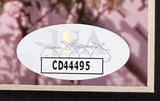 A close-up of an oval JSA authentication sticker with a signature and CD44495, featured on the Sports Integrity Jim Carrey Signed Framed 8x10 The Truman Show Photo.