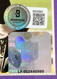 Close-up of the Sports Integrity Joe Flacco Signed Framed 8x10 Baltimore Ravens Photo BAS, featuring an NFL hologram sticker and Beckett authenticated autograph sticker with QR code and serial numbers. Football and text appear in the background.