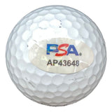 A John Daly signed Titleist Pro V1 golf ball by Sports Integrity with a PSA/DNA sticker labeled PSA in blue and red letters and AP43648 printed below it, placed on the dimpled surface of the white ball.