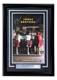 The Jonas Brothers Signed Framed 11x17 The Album Poster by Sports Integrity features the trio at a diner counter with their backs to the camera, autographed and includes a plaque listing Nick, Joe, and Kevin.