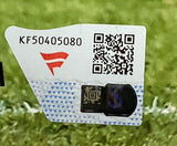 A close-up of a white sticker with a red logo, serial number KF50405080, QR codes, and a black security chip on green grass, verifying a Jonathan Taylor Signed Framed 8x10 Indianapolis Colts Photo from Sports Integrity.
