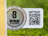 Close-up of a Beckett Witness Autograph authentication sticker with serial number 1W775307 and QR code on the Jordan Love Signed Framed 16x20 Green Bay Packers Photo by Sports Integrity, shown on a glossy surface with a green background.