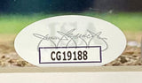 A close-up of the oval authentication sticker featuring a signature and code CG19188 on the Sports Integrity Kyle Schwarber Signed Framed 16x20 Philadelphia Phillies City Connect Photo JSA.
