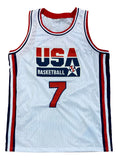 The Larry Bird Custom Olympic Basketball Jersey by Sports Integrity is a white jersey with red and blue trim, featuring "USA BASKETBALL" in bold letters, a star logo, and the number 7 on the front.