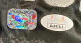 Close-up of two authentication stickers on the Mike Tyson Signed Framed Custom Black Baddest Man Boxing Trunks by Sports Integrity: a colorful holographic Fiterman Sports sticker with "GENUINE" in red and an oval USA sticker showing code WA885244 in black.