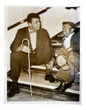 Two men converse on stairs in the Muhammad Ali VINTAGE 1960s 7x9 Hotel Theresa UPI Press Photo by Sports Integrity—one in a suit with a bow tie and cane, the other smartly dressed, smiling with one knee raised.