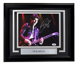 The Sports Integrity Nick Jonas Signed Framed 8x10 Photo features Nick Jonas playing guitar on stage, his autograph, and a plaque, all authenticated by PSA/DNA.