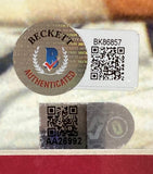 Close-up of two authentication stickers with QR codes on a Nolan Ryan Signed Framed 8x10 Texas Rangers Ventura Fight Photo BAS by Sports Integrity, featuring a circular Beckett Authenticated sticker and a rectangular AA26992 sticker.