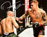 Two MMA fighters face off intensely in the cage as one throws a punch and the other defends. This is captured in the Dustin Poirier Signed 8x10 UFC Fight vs Conor McGregor Photo by Sports Integrity, complete with PSA/DNA authentication.