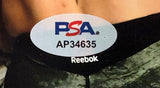 Close-up of a PSA authentication sticker labeled AP34635 on a Dustin Poirier Signed 8x10 UFC Fight vs Conor McGregor Photo by Sports Integrity, with part of the word "Reebok" visible below.