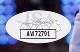 A Post Malone Signed Framed 8x10 Photo by Sports Integrity features a white oval JSA hologram sticker with a black signature, faded JSA letters, and the bold code AW72791; blue and black tones appear in the blurred background.