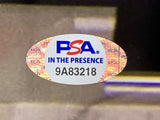 A close-up of an oval PSA holographic sticker labeled “PSA IN THE PRESENCE 9A83218” used to authenticate a Rainn Wilson Signed Framed 11x14 The Office Dwight Interim Mgr Photo by Sports Integrity; background is out of focus.