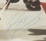 A close-up of Reggie Leach holding a hockey stick on an 8x10 Philadelphia Flyers photo, featuring his large blue autograph diagonally across the image. Product by Sports Integrity, JSA AL44173 authenticated.