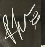A white, stylized autograph with bold, looping strokes is displayed on a dark background of the Rhea Ripley Signed Framed WWE Judgement Day Vest from Sports Integrity. The signature stands out but makes the name hard to identify.