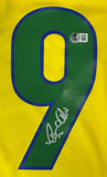 The Sports Integrity Ronaldo Signed Brazil Nike Soccer Jersey BAS features a yellow design, large green and blue number 9, silver autograph, and an authentication sticker with a QR code above the number.