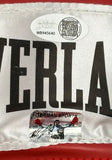 Close-up of a fabric label on the Sports Integrity Mike Tyson Signed Red Everlast Right Hand Boxing Glove, showing bold black letters, two QR code authenticity stickers with serial numbers, a signature, and small graphic.