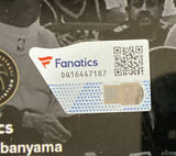 A close-up of a Sports Integrity Fanatics authenticity sticker with a QR code, serial DQ16447187, and holographic feature on the Victor Wembanyama Signed Framed 16x20 San Antonio Spurs Dunk Photo. Black background, faint text/images behind.