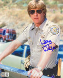 The Sports Integrity Larry Wilcox Signed 8x10 CHIPS Sunglasses Photo BAS ITP shows a man in a tan police uniform with aviator sunglasses by a railing, a green car and van behind, and features Larry Wilcox’s blue signature.