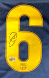 A yellow number 6 is printed on a blue Xavi Signed Barcelona Nike 2009 UEFA Champions League Soccer Jersey BAS by Sports Integrity, featuring a black autograph and an authenticity sticker with QR code at the bottom.
